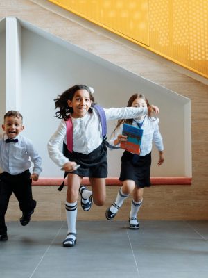 Happy school children in uniforms running energetically indoors, expressing excitement.